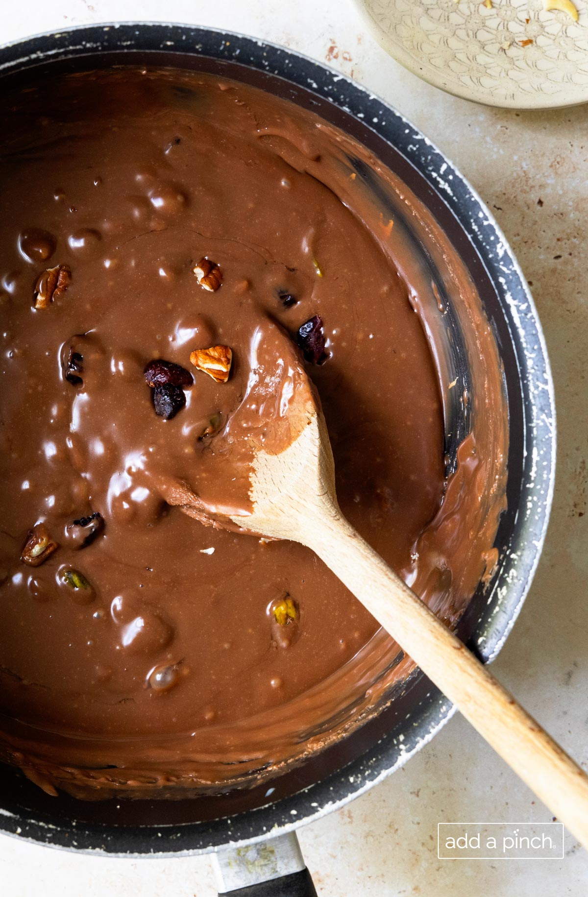 Wooden spoon stirring nuts and dried fruit into melted chocolate.