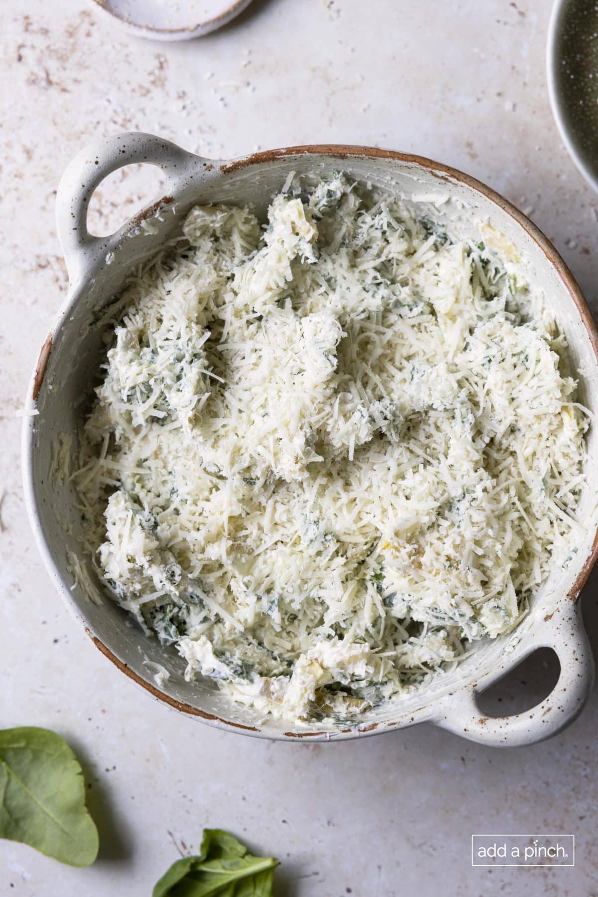 Dip in round baking dish is covered in shredded parmesan and ready to be baked.