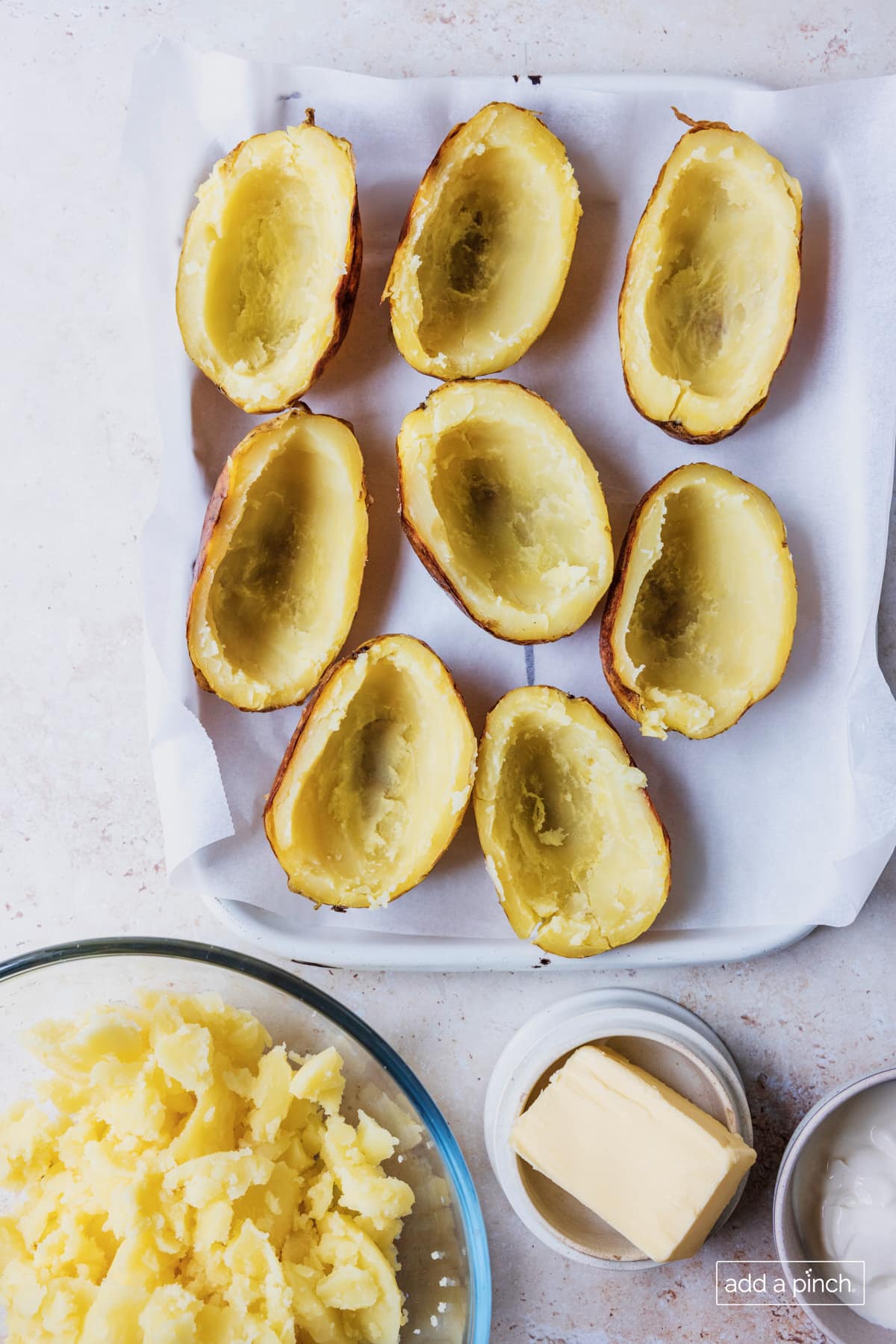 Photo of potatoes with the interior scooped out and in a mixing bowl with butter and sour cream on the side.