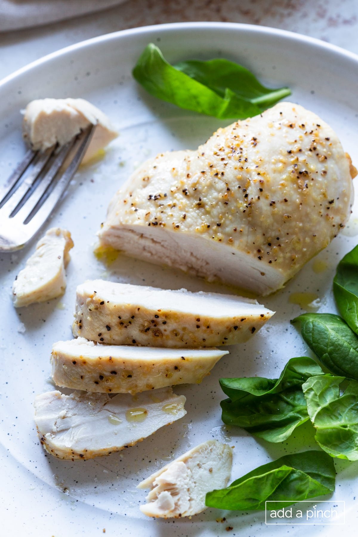 Photo of cooked chicken breast that's been sliced on a white plate with bite of chicken on a fork.