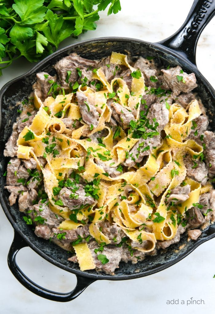 Photograph of beef stroganoff in a skillet topped with chopped fresh parsley.