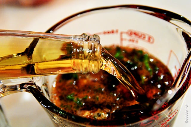 Beer being poured into a glass measuring cup with other marinade ingredients.