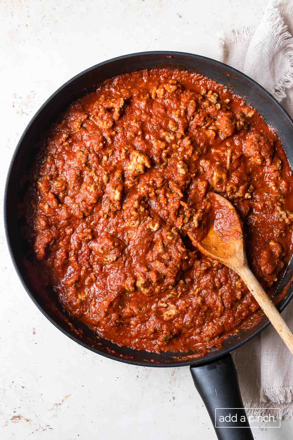 Photograph of lasagna meat sauce in a skillet with a wooden spoon.
