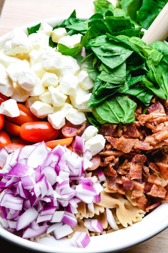 Chopped ingredients on top of farfalle pasta to make a salad.