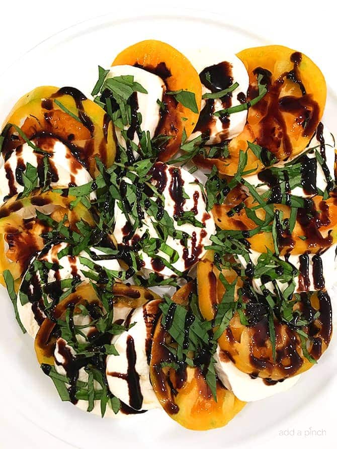 Yellow heirloom tomato slices layered with thick slices of mozzarella cheese and topped with ribbons of fresh basil and balsamic glaze on a white platter.