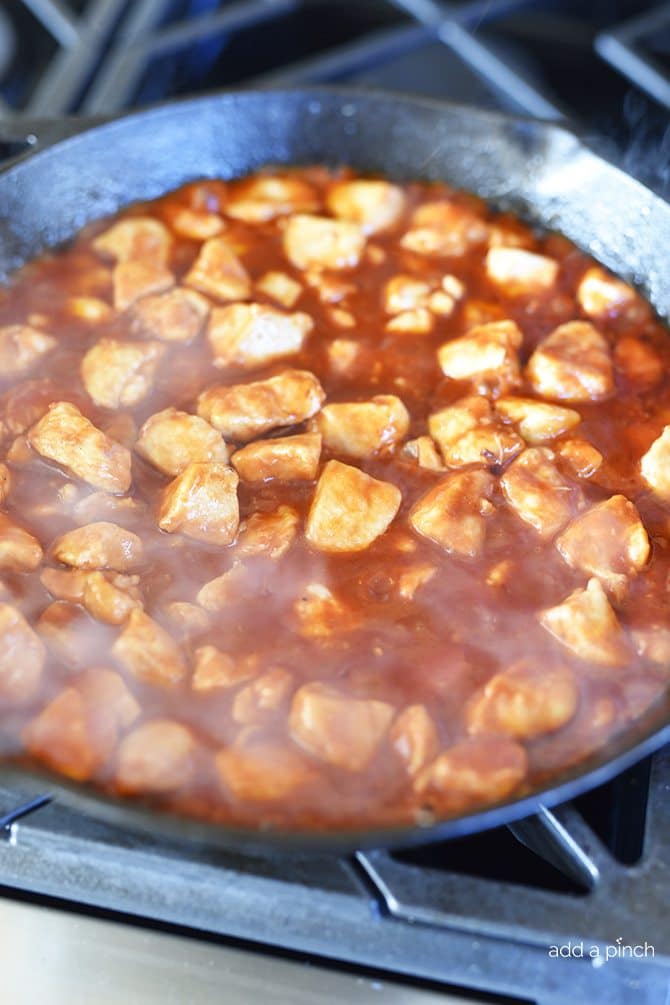 Chicken breast pieces are cooking in a sauce in an iron skillet.