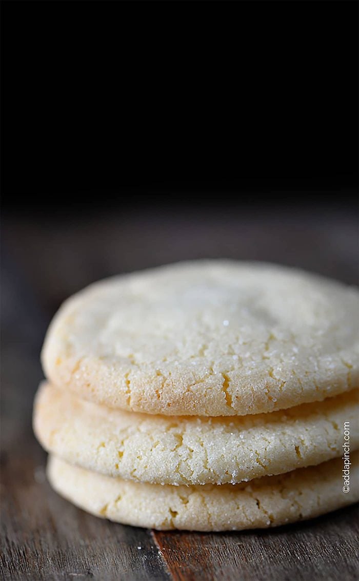 Stack of three Chewy Sugar Cookies that have been rolled in granulated sugar. On wooden board with sugar crystals on board.