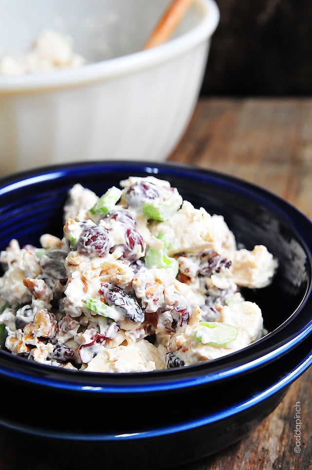 Photograph of chicken with grapes in a blue bowl on a wooden background.