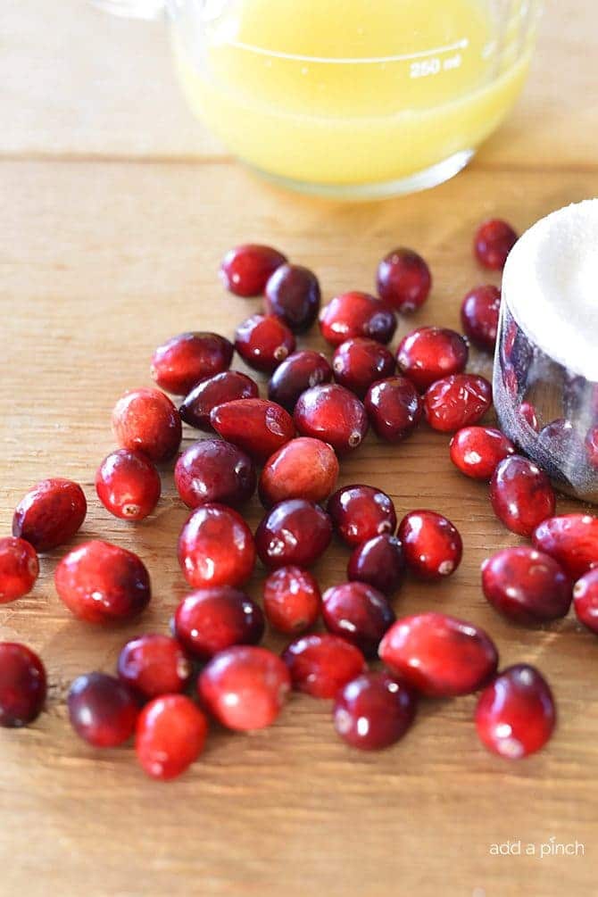 Ingredients to make homemade cranberry sauce: fresh whole cranberries, fresh orange juice, and sugar on wooden board.