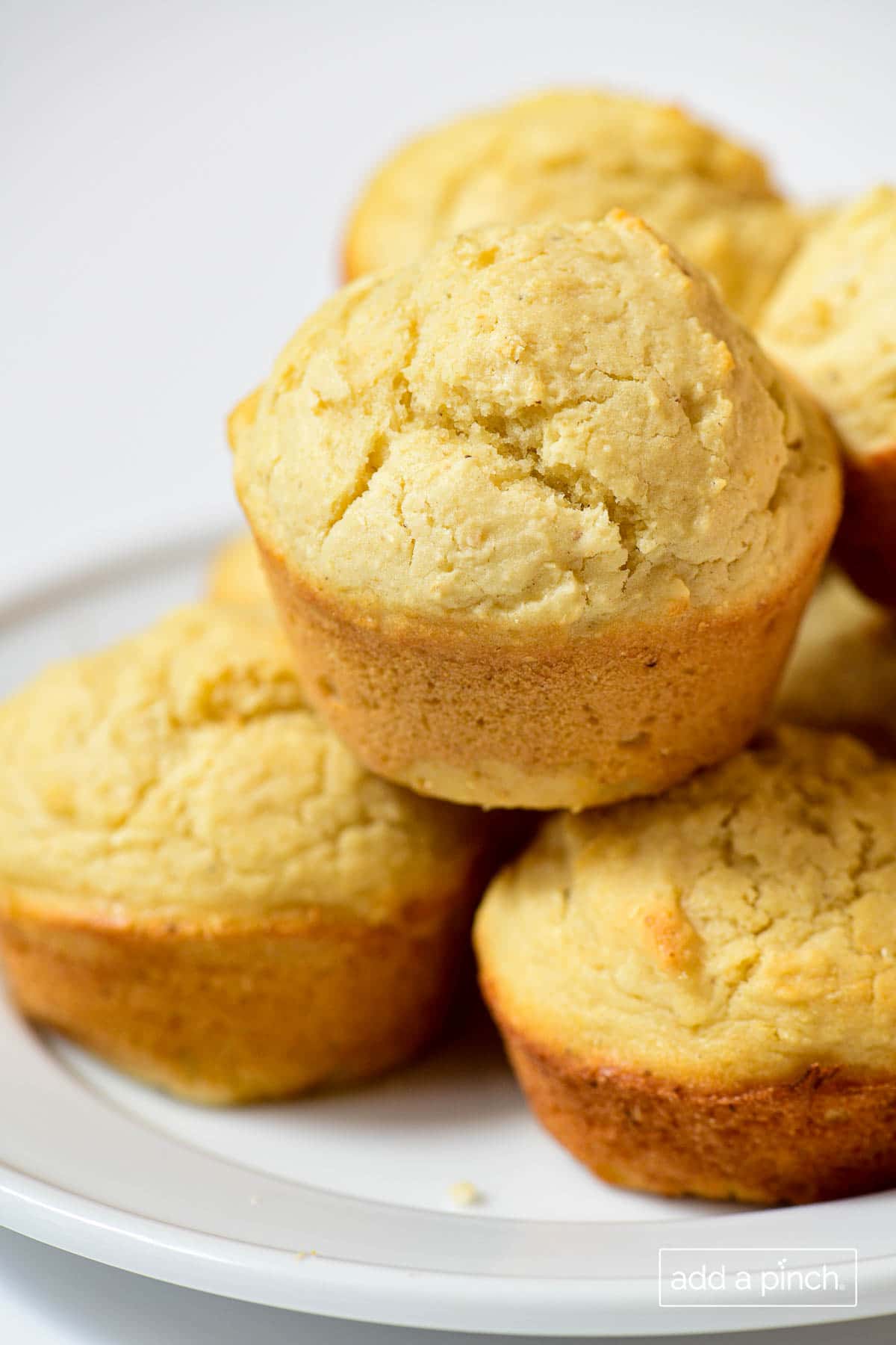 Closeup photo of stack of golden brown baked cornbread muffins on a white plate and white background.