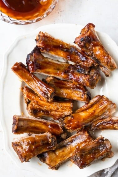 Photo of BBQ ribs on a white platter on a white background.