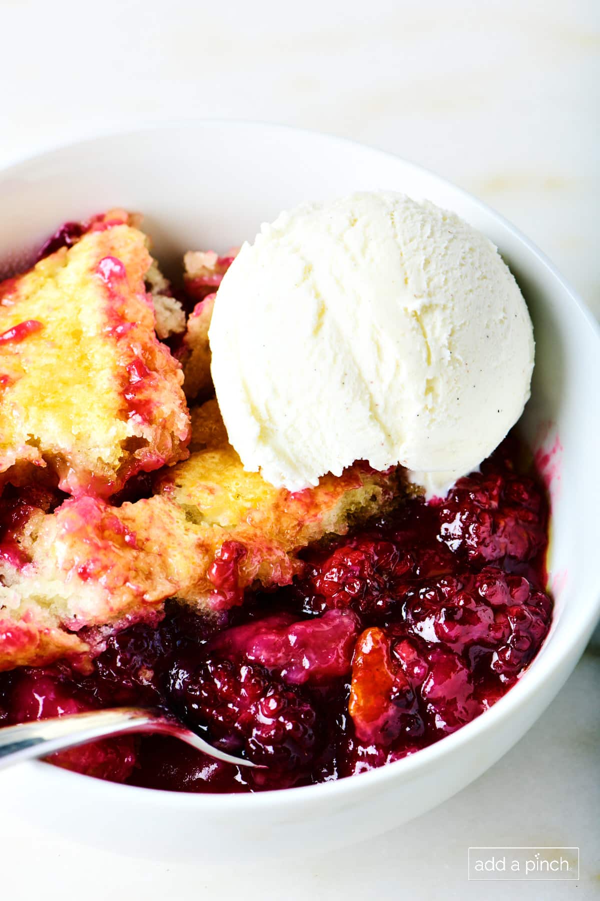 Vanilla ice cream on top of blackberry cobbler in a white bowl.
