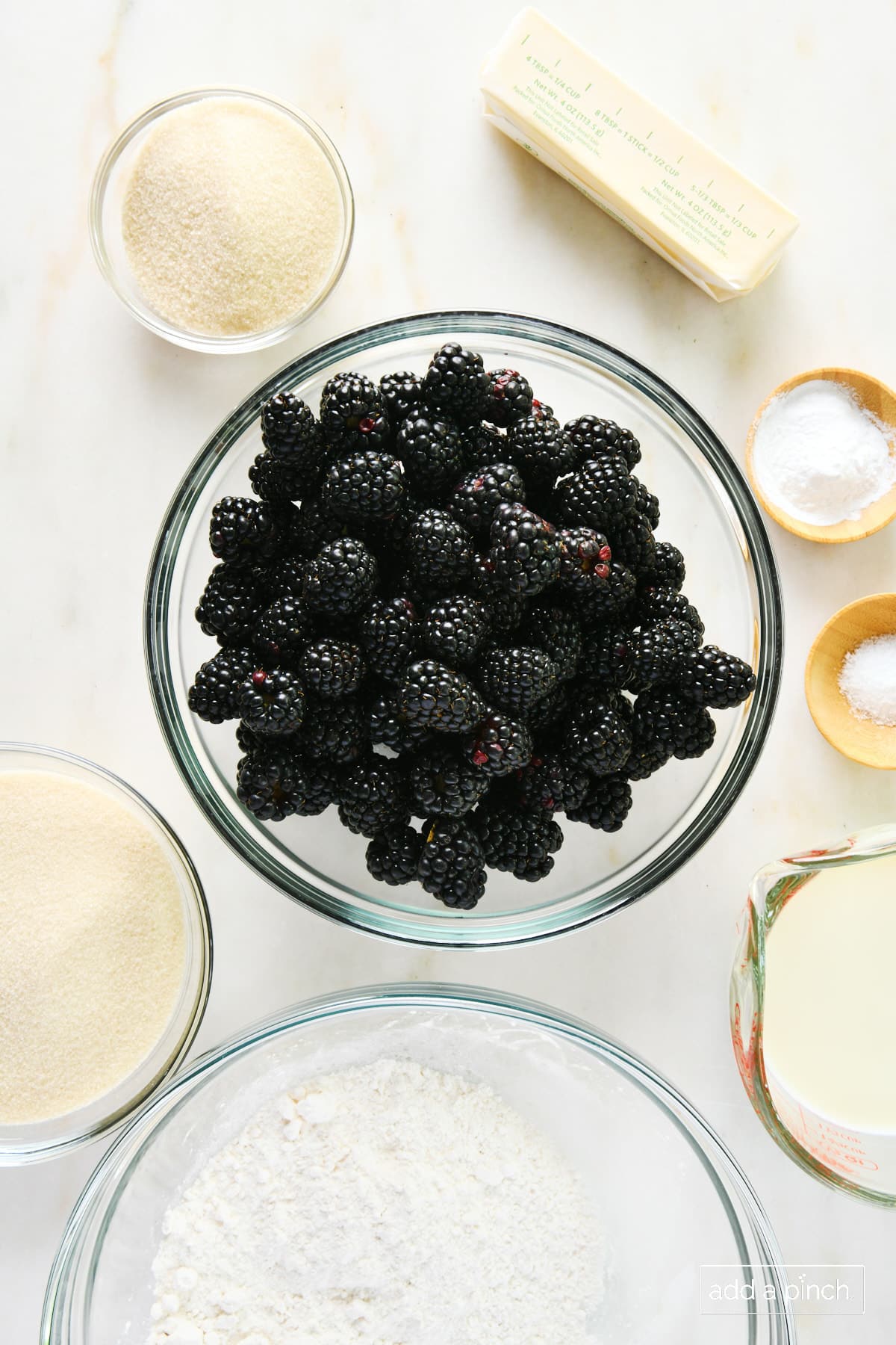 Ingredients to make blackberry cobbler - fresh blackberries and butter, and baking ingredients - on a marble surface.