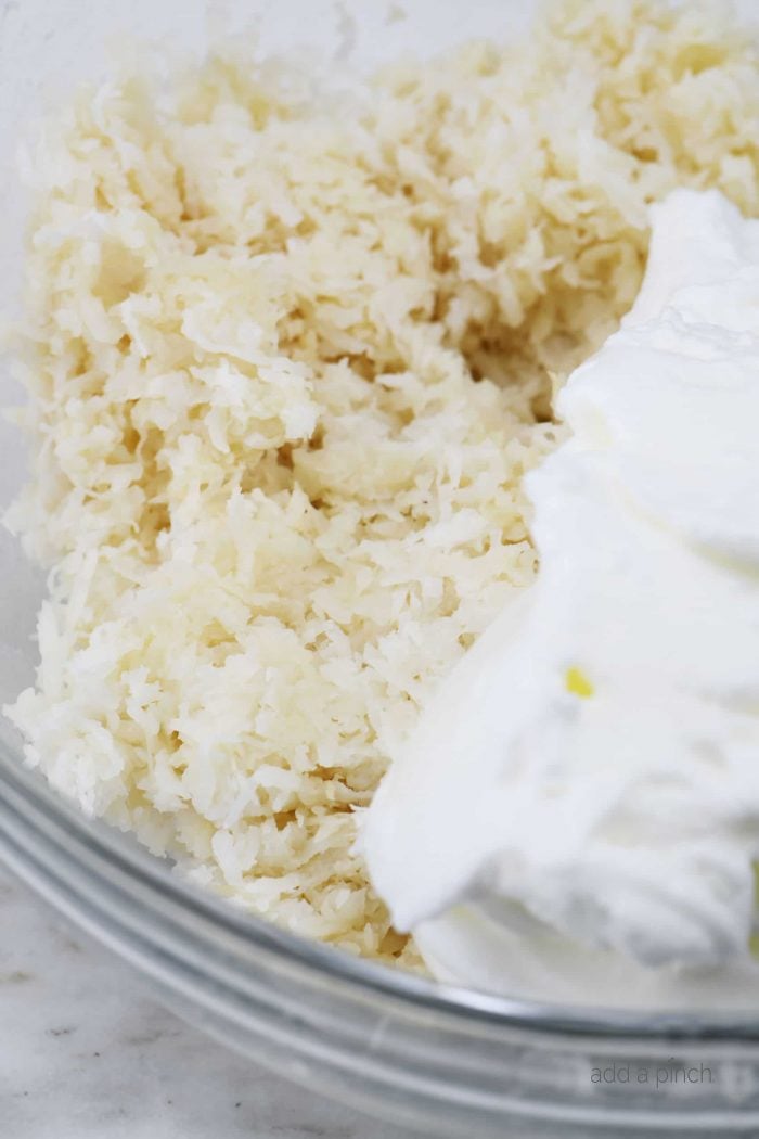 Glass bowl with coconut mixture and fluffy beaten egg whites, on marble counter.