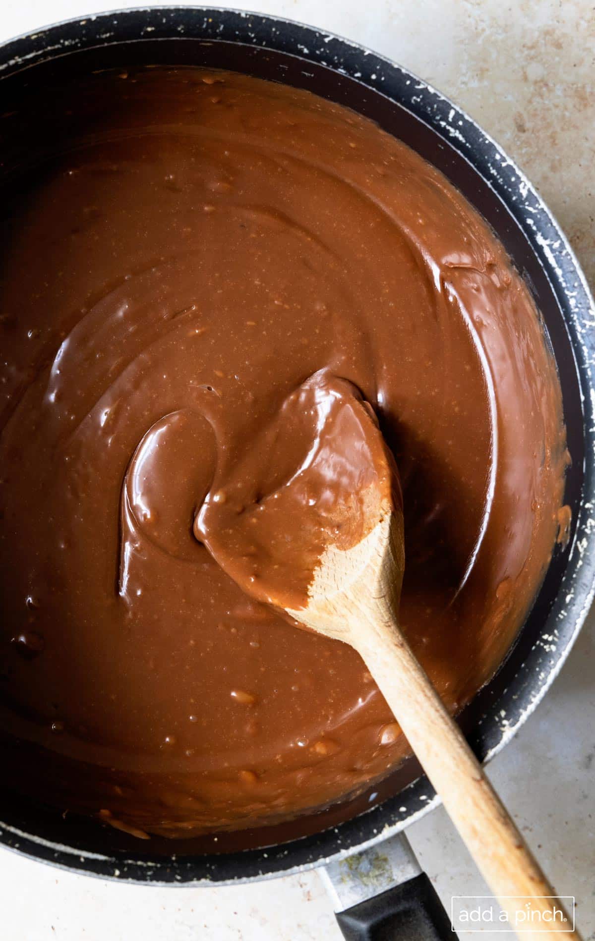Photo of melted chocolate in a saucepan with a wooden spoon ready to be poured into a prepared pan.