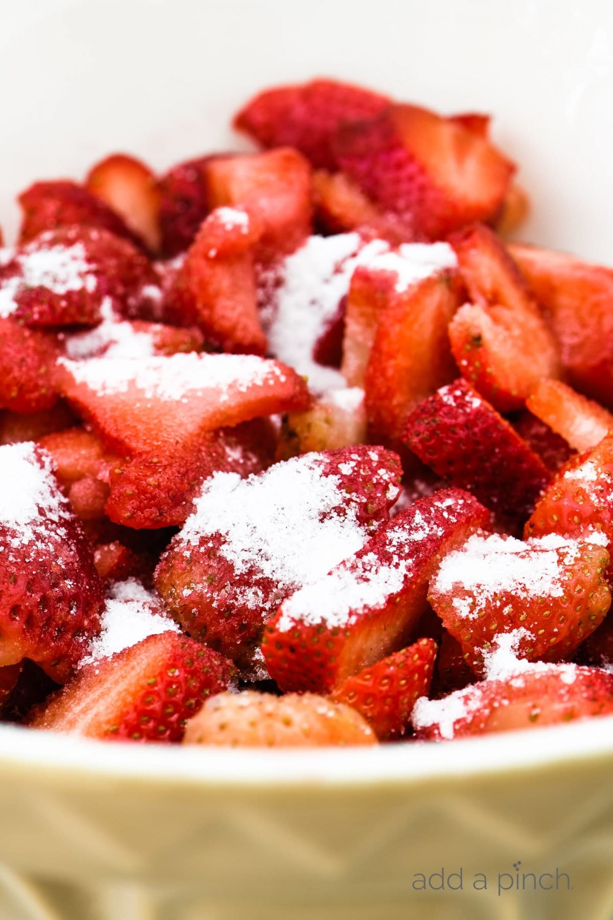 Sliced strawberries with sugar in a large white bowl.