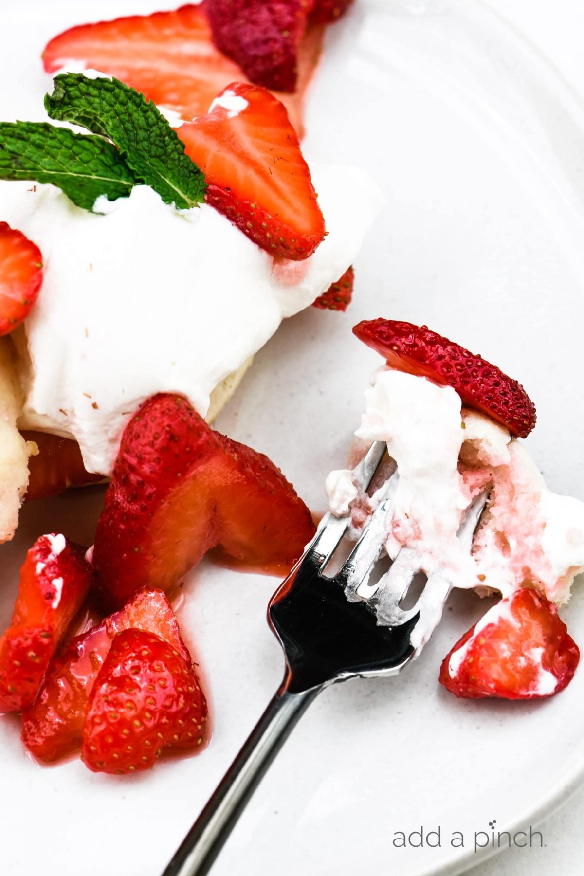 Strawberry shortcake, whipped cream, and strawberry slices on a white plate with a fork.