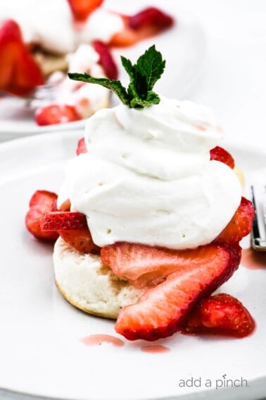 Strawberry shortcake topped with homemade whipped cream and mint sprig on a white plate.