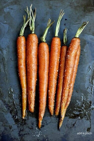 Baking pan holds several roasted carrots with green tops.