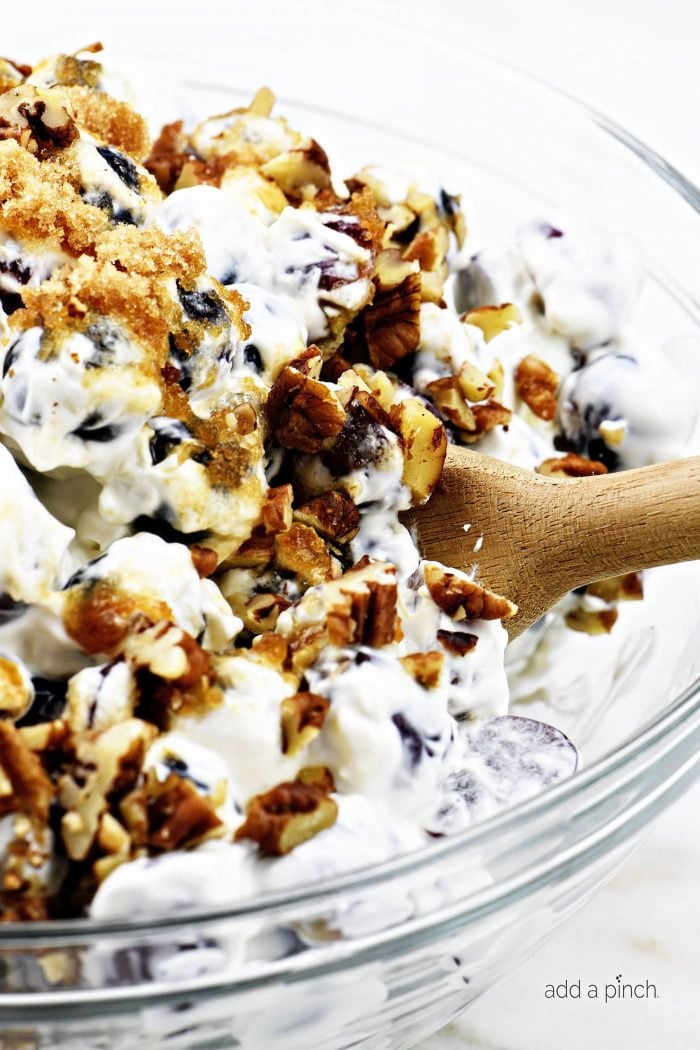 Serving grape salad from a glass bowl with a wooden spoon.