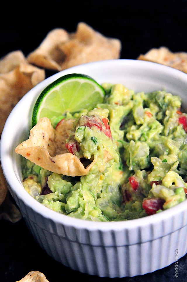 guacamole-DSC_1685 White dish of guacamole with a lime slice and a tortilla chip.
