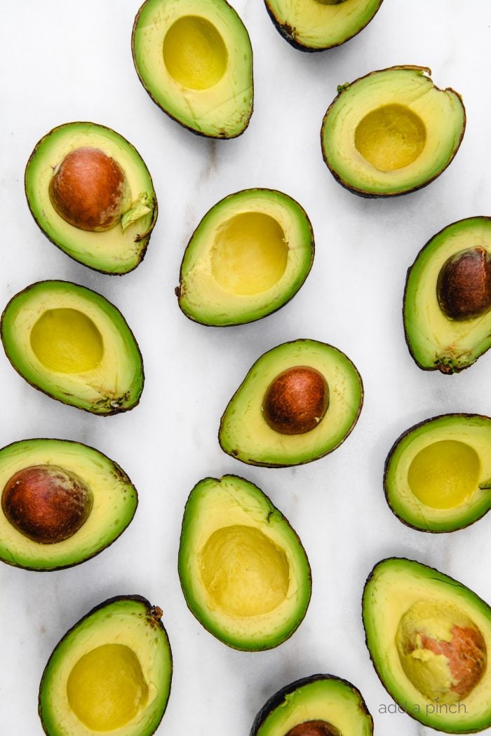 Several avocados are cut in half showing the perfect amount of ripeness to use them. Some avocado halves still hold their pits.