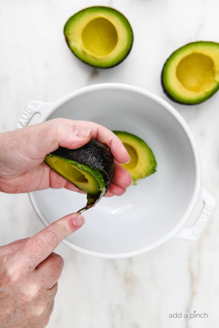 White bowl on marble countertop with fresh avocado being scooped into it with a spoon.