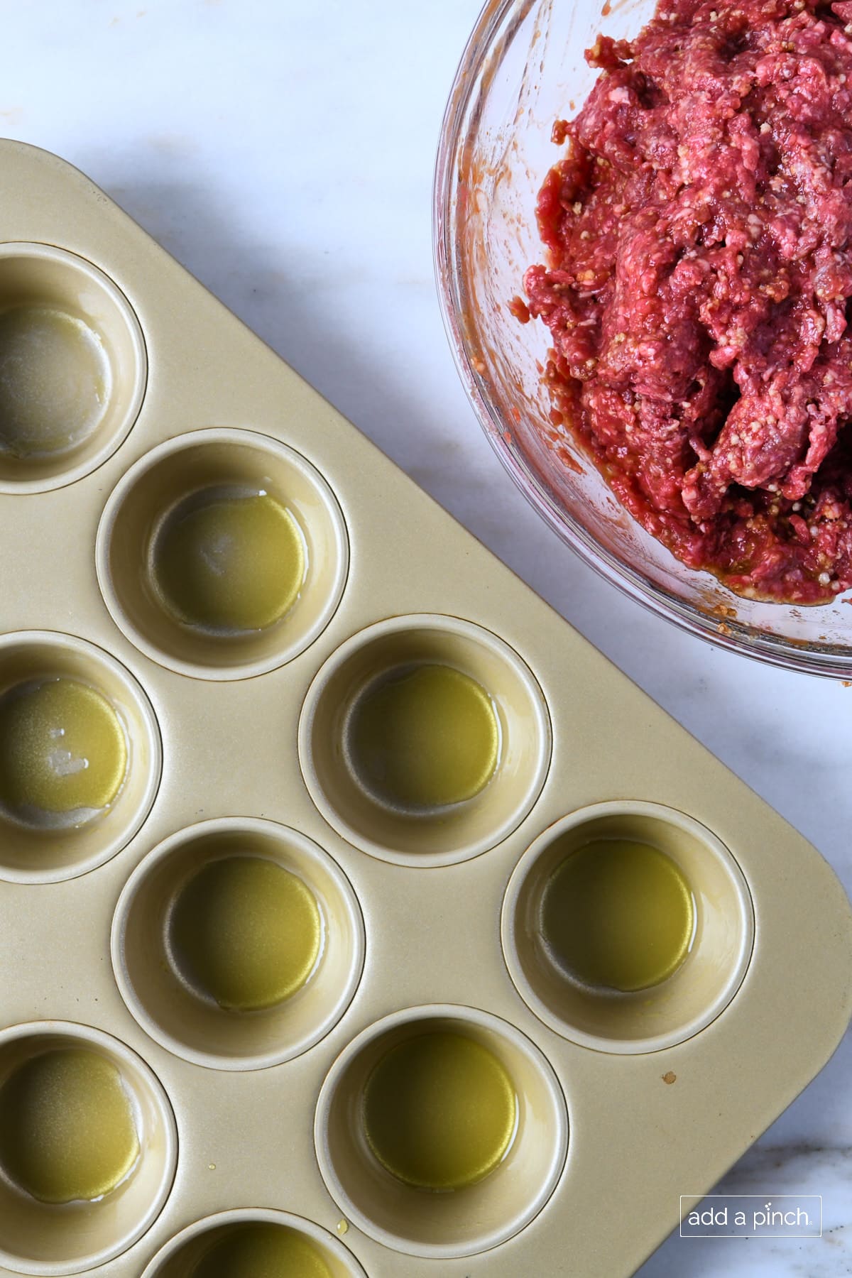 Muffin pan coated with olive oil and meatloaf mixture in a glass bowl.