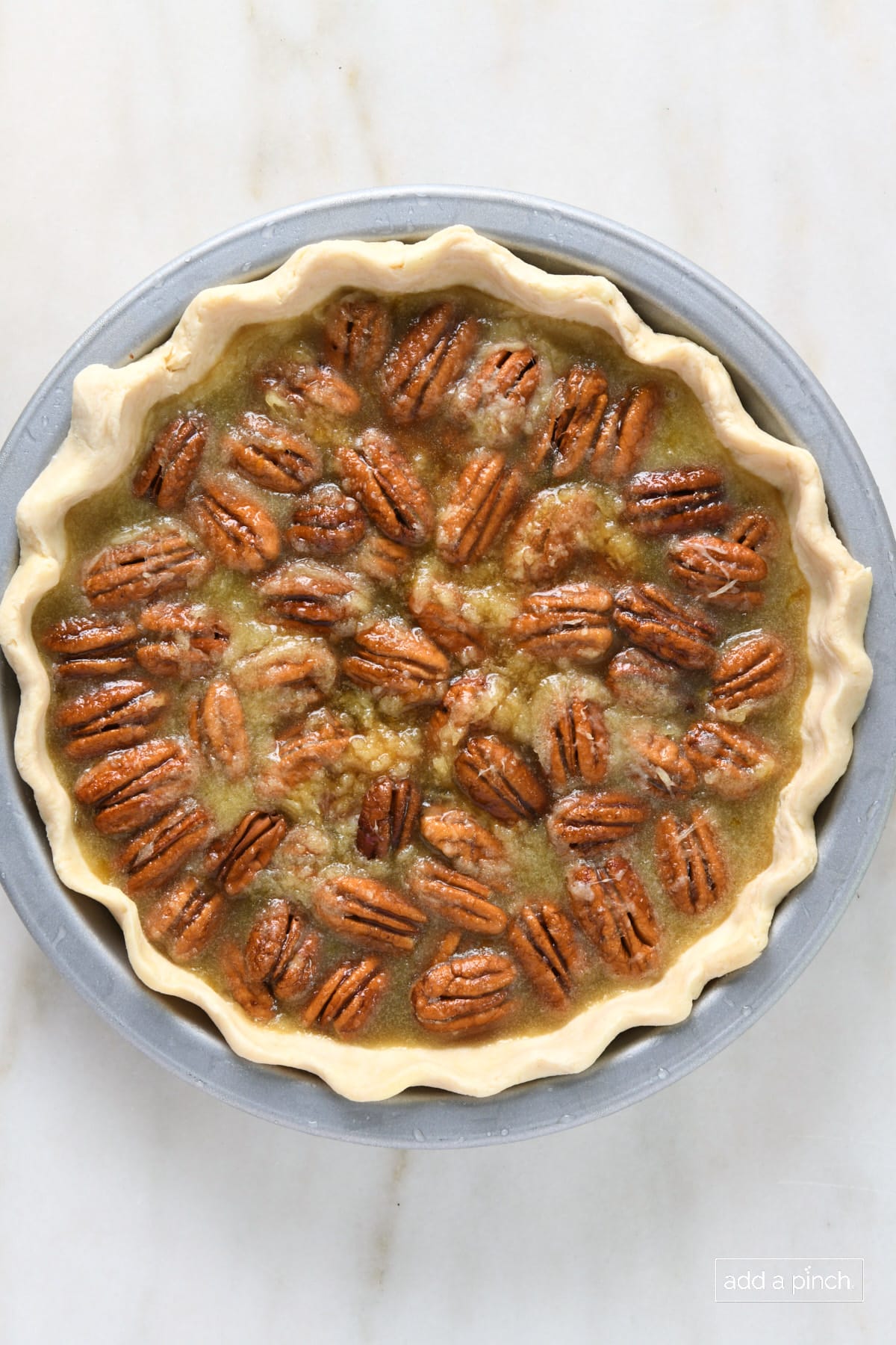Pie plate with unbaked pie - a homemade pie crust with hand-fluted edge filled with pecan pie filling containing pecan halves.