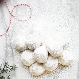 Powdered sugar covered cookies on a marble countertop with greenery and twine.