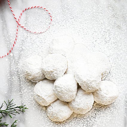 Powdered sugar covered cookies on a marble countertop with greenery and twine.