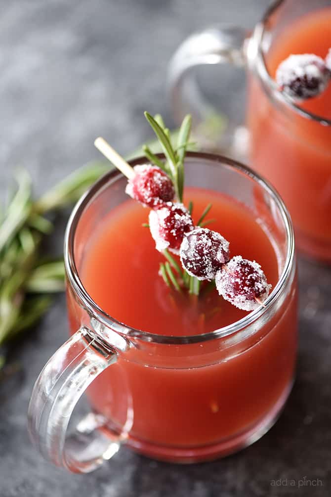 Cup of red pomegranate cranberry cider with sugared cranberries on a pick and rosemary for garnish.