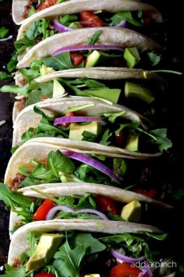 Line of colorful tacos filled with beef, tomatoes, cheese, lettuce and onions.
