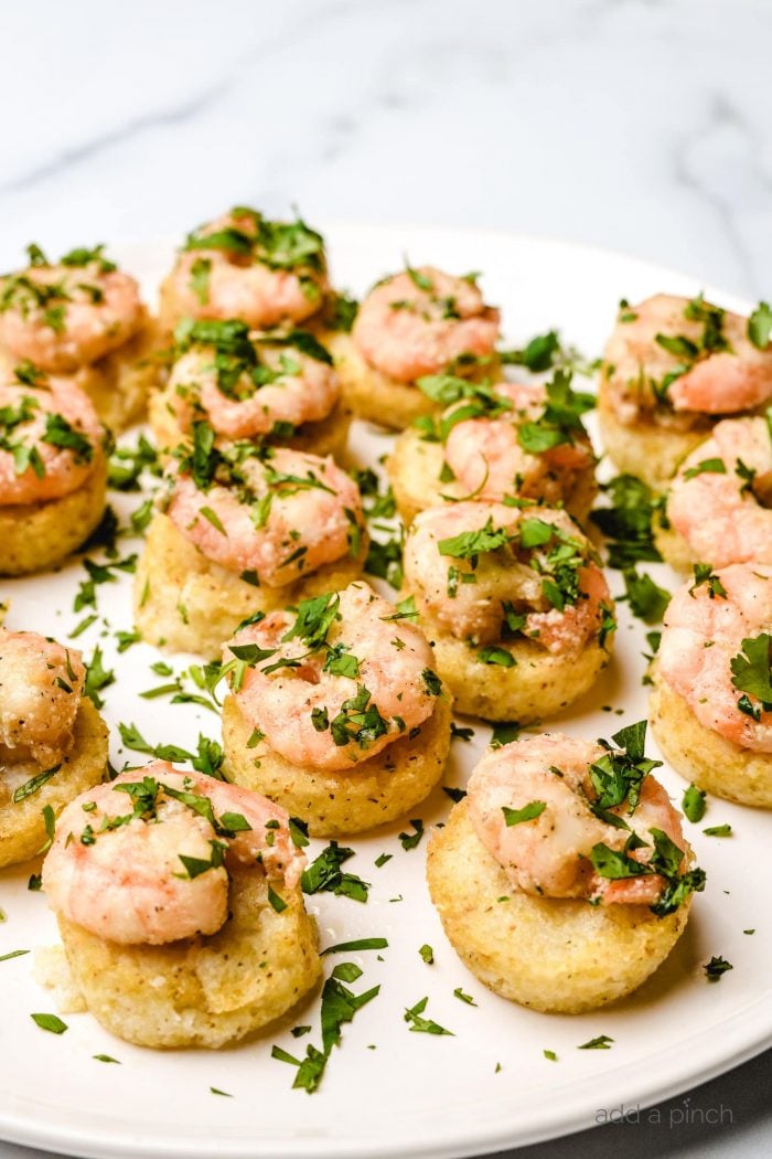 Several parsley-topped shrimp and grits bites served on a white plate.