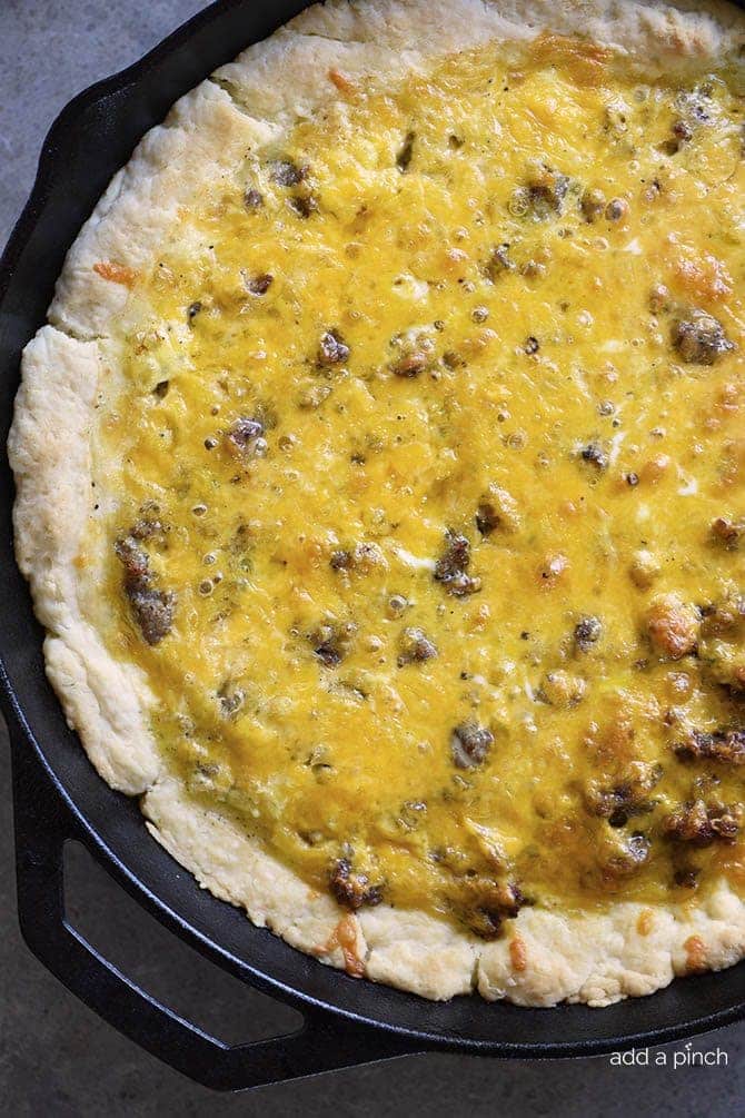 A large cast iron skillet holds a biscuit crust filled with a cheesy sausage and cheddar quiche.