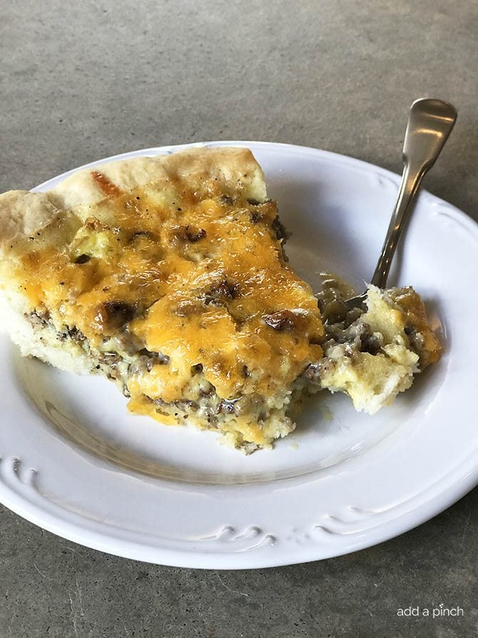 Slice of quiche with sausage and cheese on a white plate with a fork.