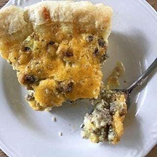 Photo of sausage cheddar quiche with pastry crust and fork with bite of quiche on white plate.