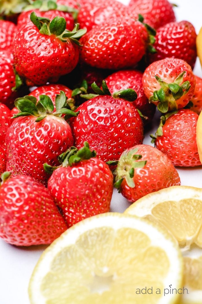 Fresh strawberries and fresh lemon slices on a white board.