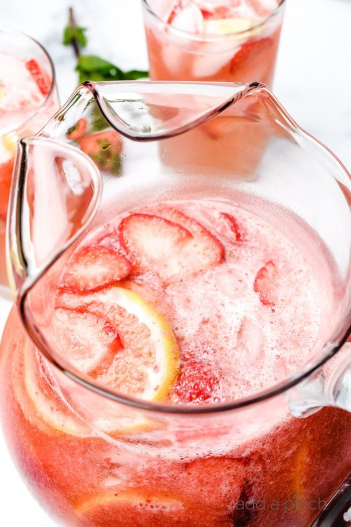 Glass pitcher and glasses of strawberry lemonade garnished with fresh strawberries and lemon slices.