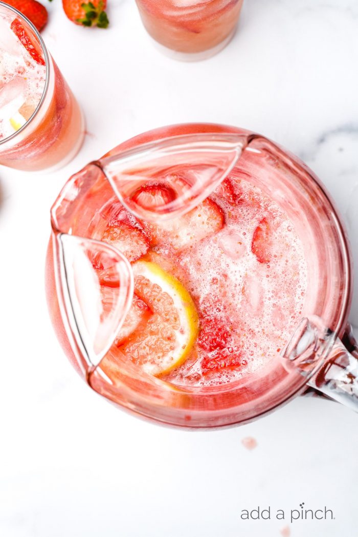 White counter with strawberry lemonade with ice and lemons.