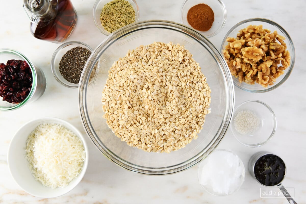 Ingredients used to make homemade granola - oats, walnuts, spices, coconut flakes, salt, coconut oil, chia seeds - on a marble surface.